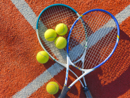 Tennis rackets and balls are arranged on a red and white court surface in the image.